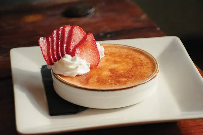 Crème brûlée topped with whipped cream and sliced strawberry